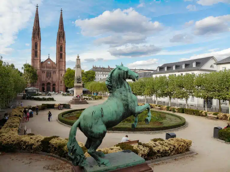 Bronze Pferdestatue mit Blick auf einen gepflegten Garten und die Türme der St. Bonifatius Kirche in Wiesbaden.